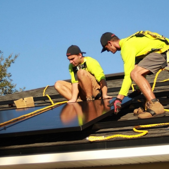 Two roofers are pulling and adjusting a solar panel on top of a roof system.